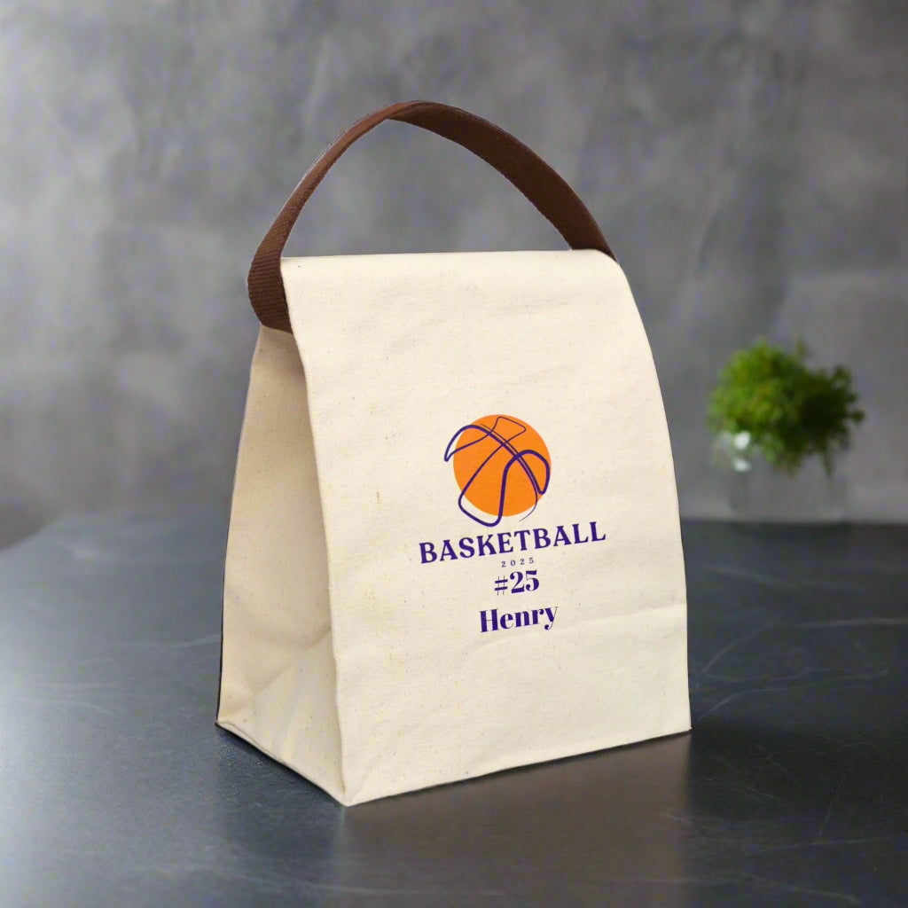 Beige lunch bag with brown handle featuring a basketball design and text on a white background
