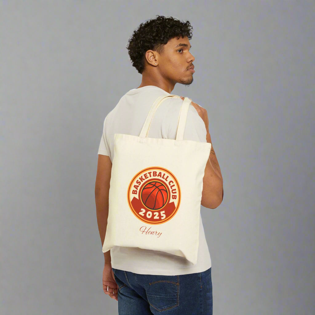 Man carrying a tote bag with a basketball club logo on a white background