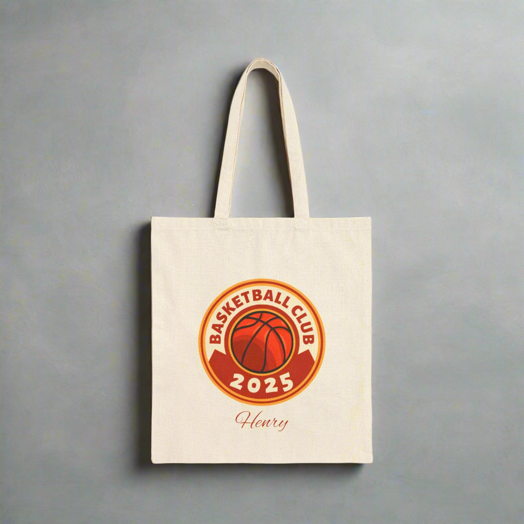 Beige tote bag with basketball club logo and text on a white background